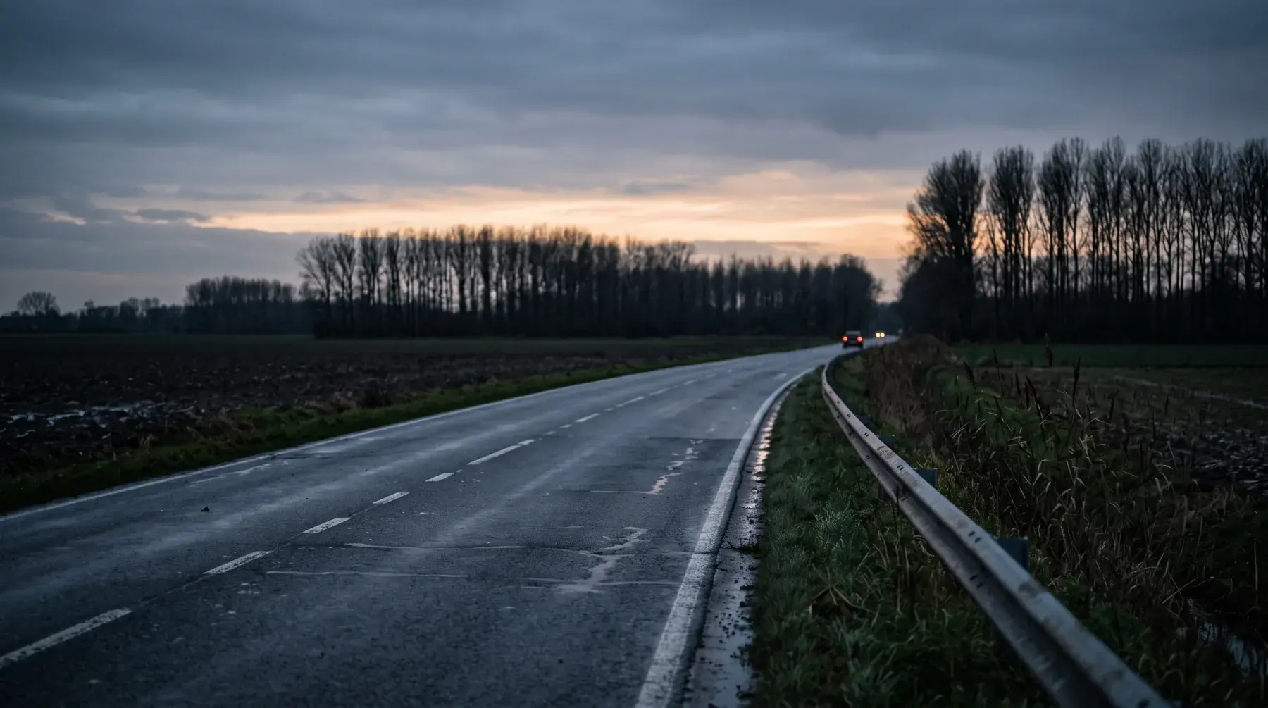 Natte landweg bij schemering met een wagen in de verte